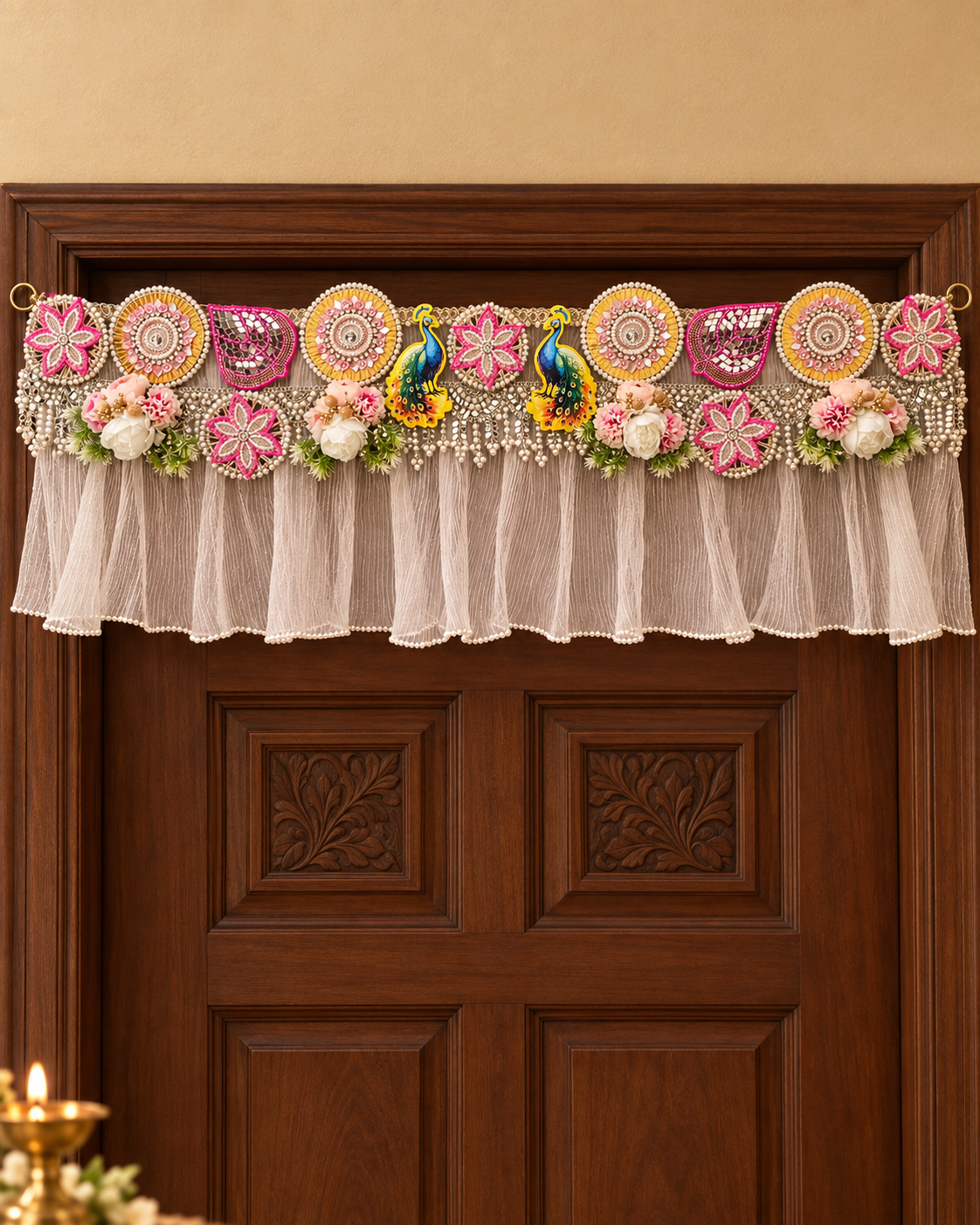 Peacock Mirror Toran hanging on a wooden main door: handmade toran with mirror work, pearls, pink floral motifs, peacocks and a sheer pleated frill