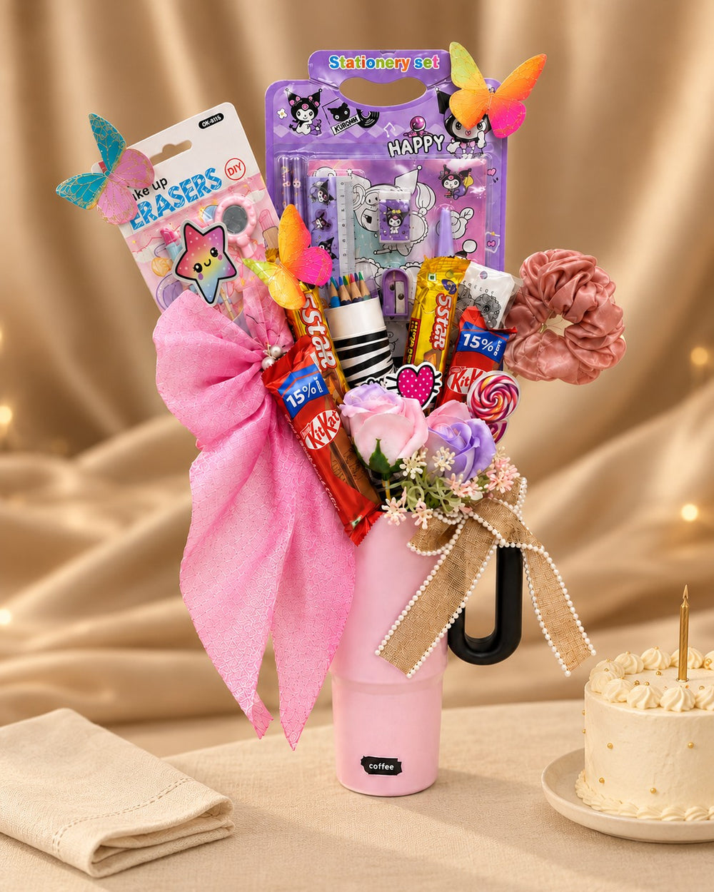 Birthday gift for her: pink tumbler hamper with stationery and chocolates beside a birthday cake