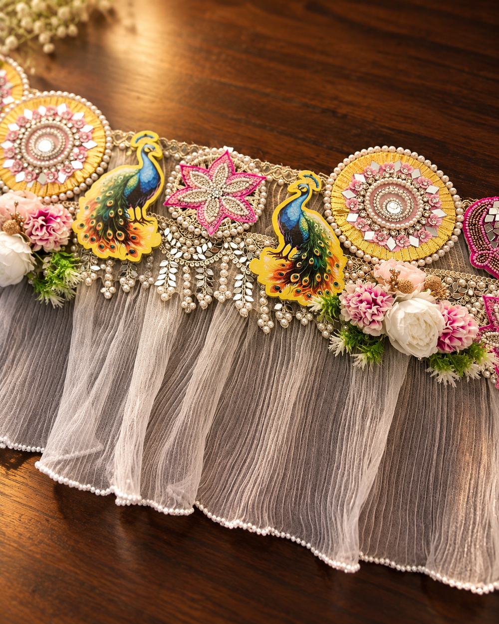 Close-up of the handmade toran: mirror and pearl medallions, embroidered pink star, two peacocks and flower clusters