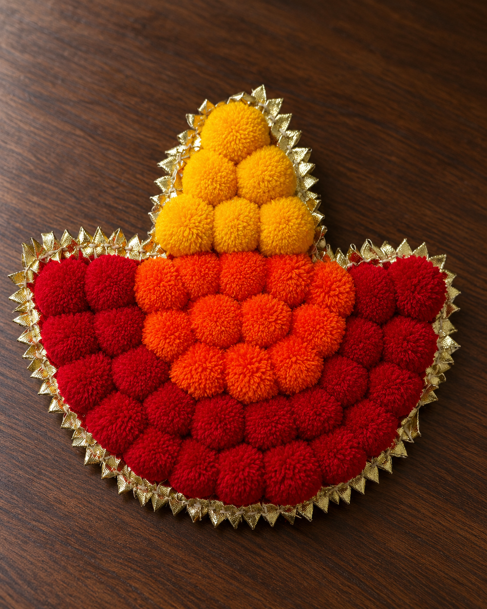 Close-up of one handmade pom-pom diya rangoli piece with a gold gota border