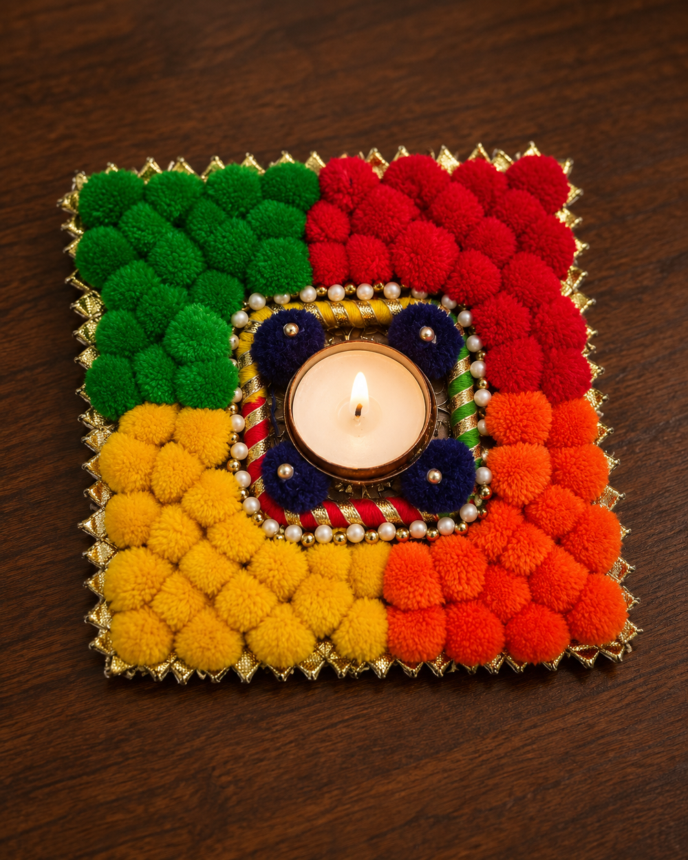 Close-up of the square rangoli piece with a lit tealight, navy pom-poms, pearls and gota